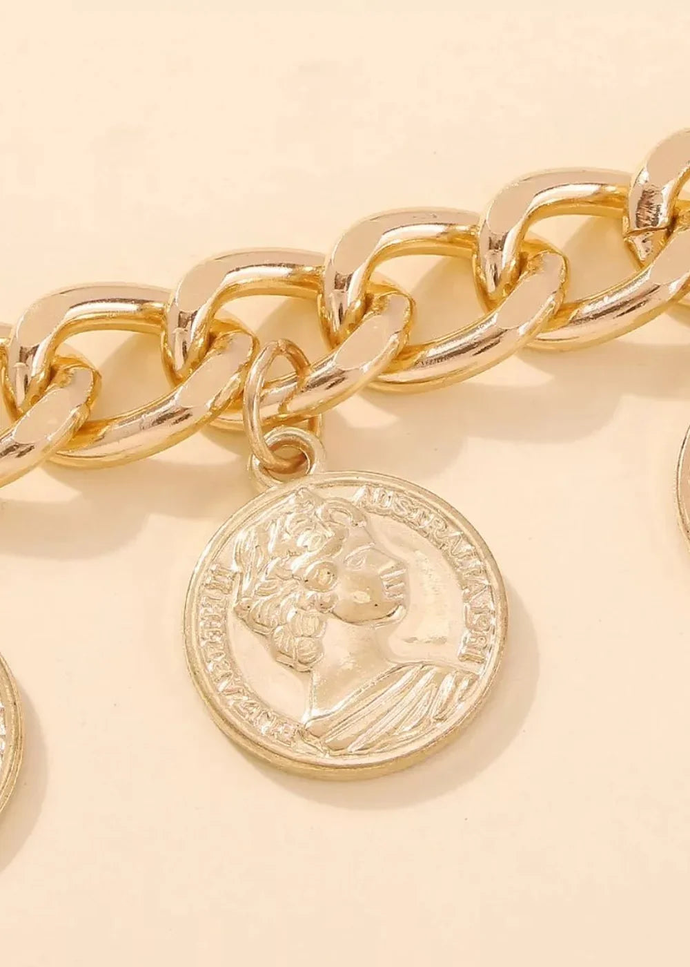 Close-up of a thick, shiny gold chain bracelet with a round coin pendant featuring a profile image.