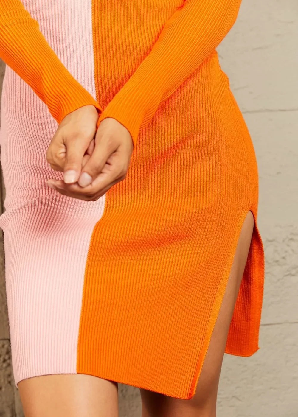 Ribbed knit sweater dress with colorblock design in bright orange and light pink, featuring long sleeves and a side slit.