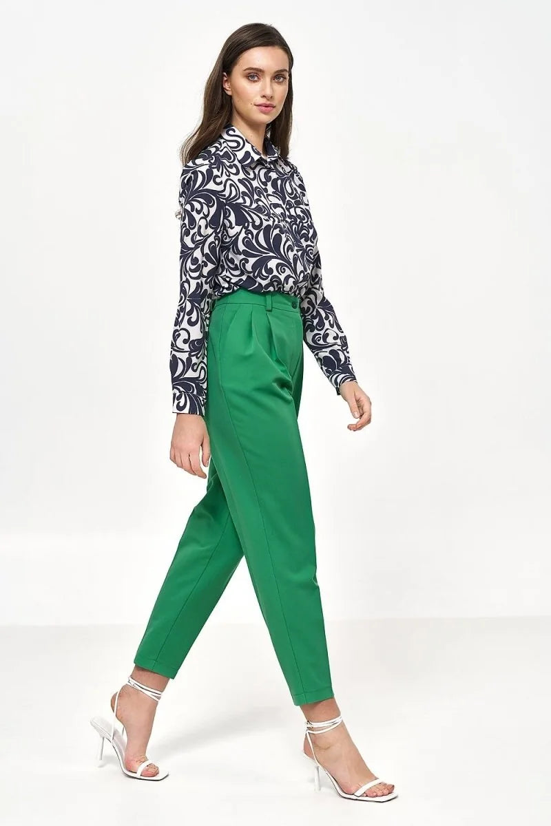 Woman in a navy and white patterned blouse and vibrant green pleated pants with white strappy heels.
