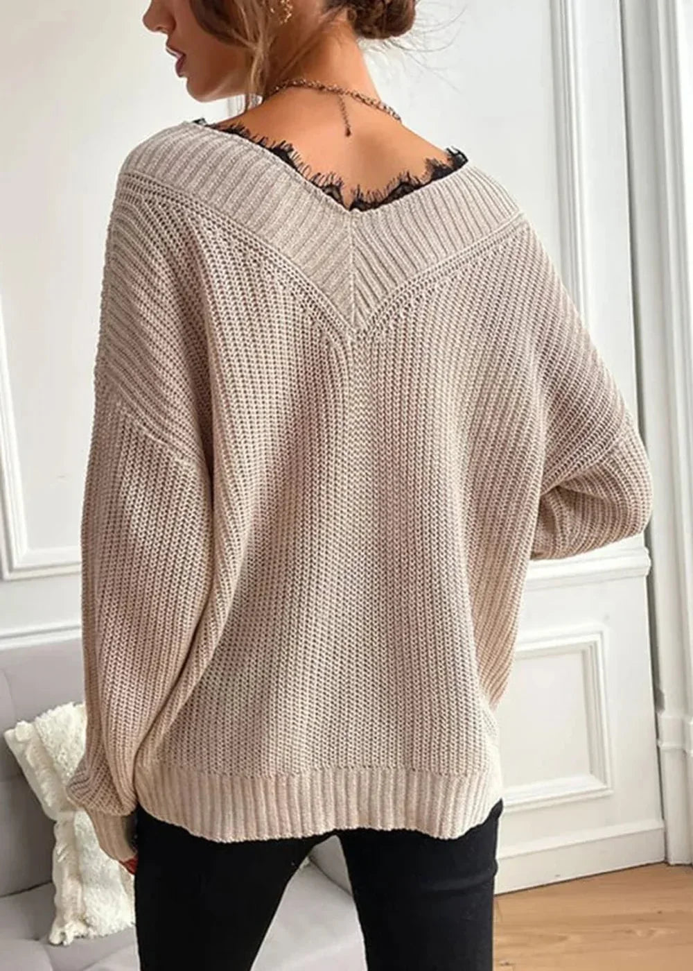 Beige knit sweater with black lace trim at V-neck, on model.