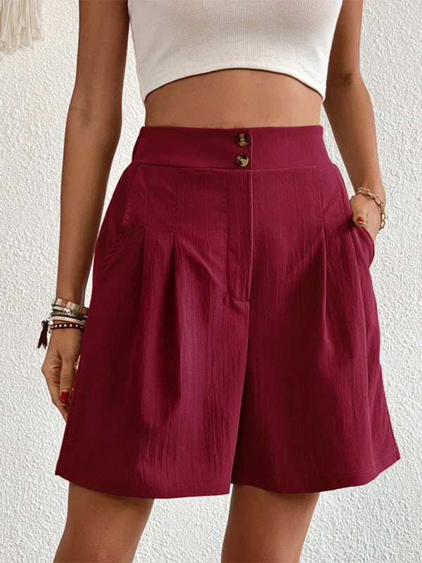 Burgundy pleated shorts with a textured fabric and gold button details, on model.