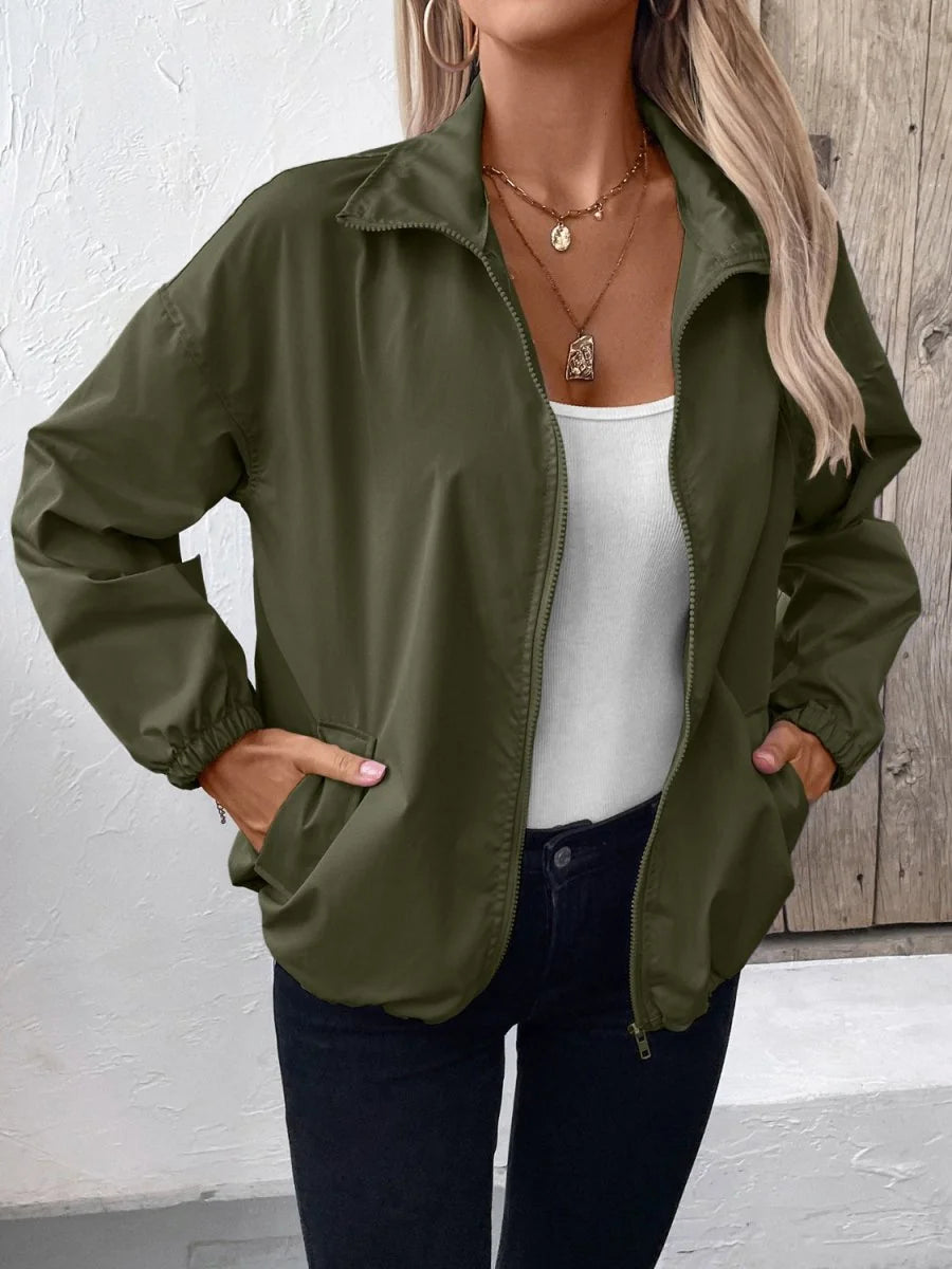 Olive green zip-up jacket with elastic cuffs and collar, worn by a model over a white top.