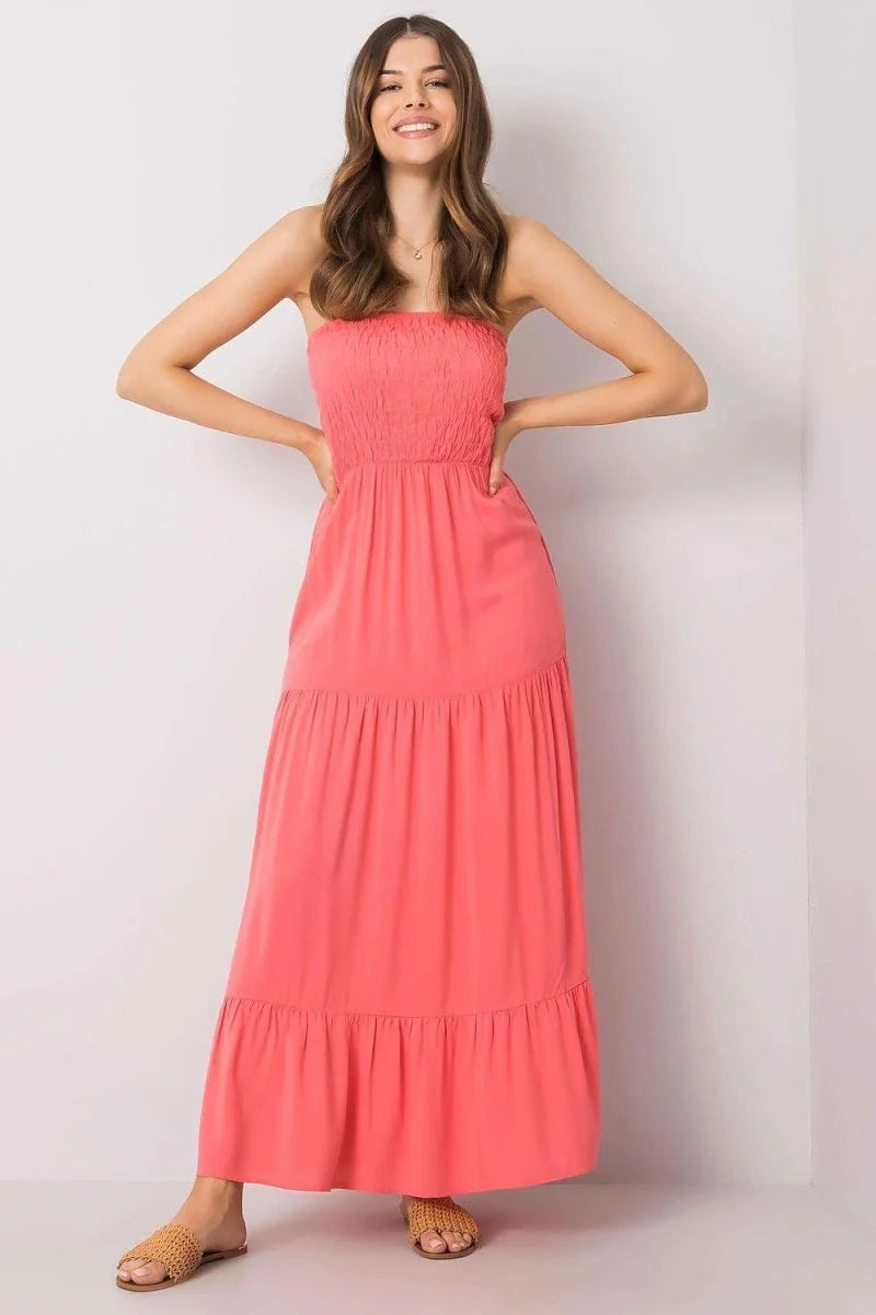 Coral strapless maxi dress with smocked bodice and tiered skirt, worn by a model.