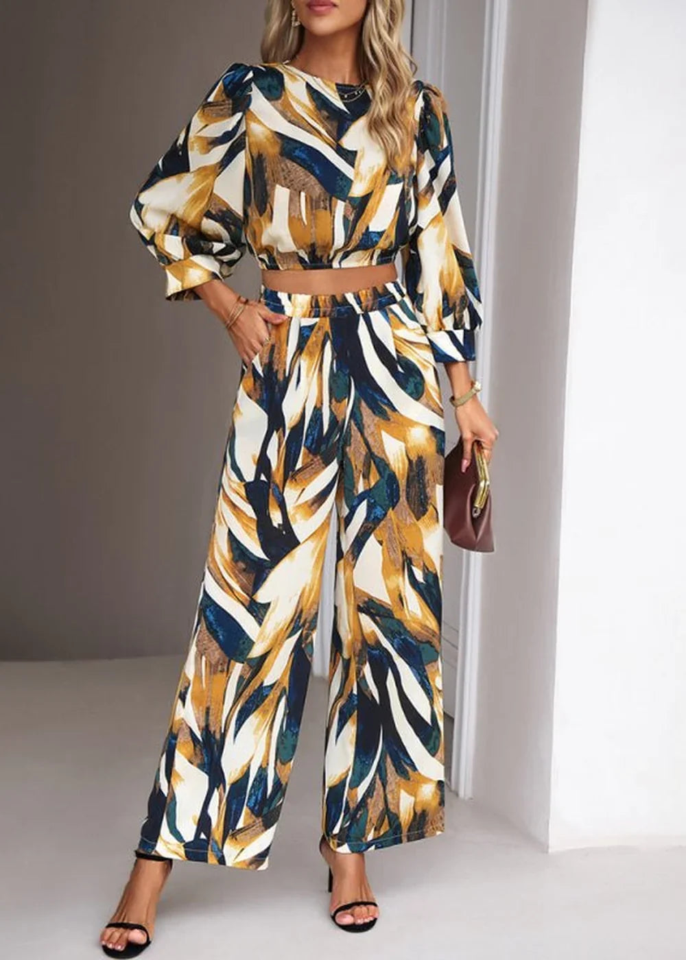 Woman in a flowing wide-leg pant suit with a bold abstract print in navy, gold, and white.