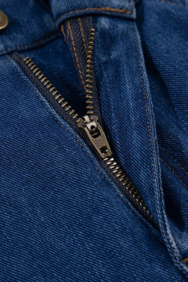 Close-up of a partially unzipped dark blue denim fly with a brass zipper.