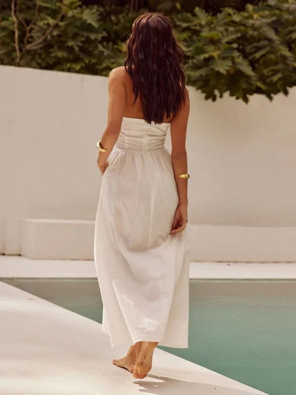 Woman in a white, strapless maxi dress with a flowing skirt walks by a pool.