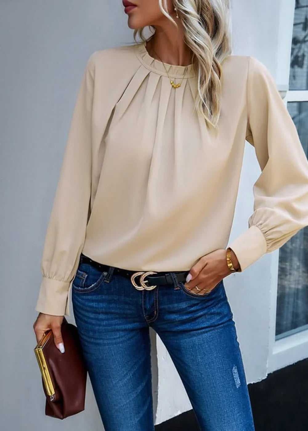 Beige pleated long-sleeve blouse with a mock neck, paired with dark wash denim jeans and a black belt with a gold double C...