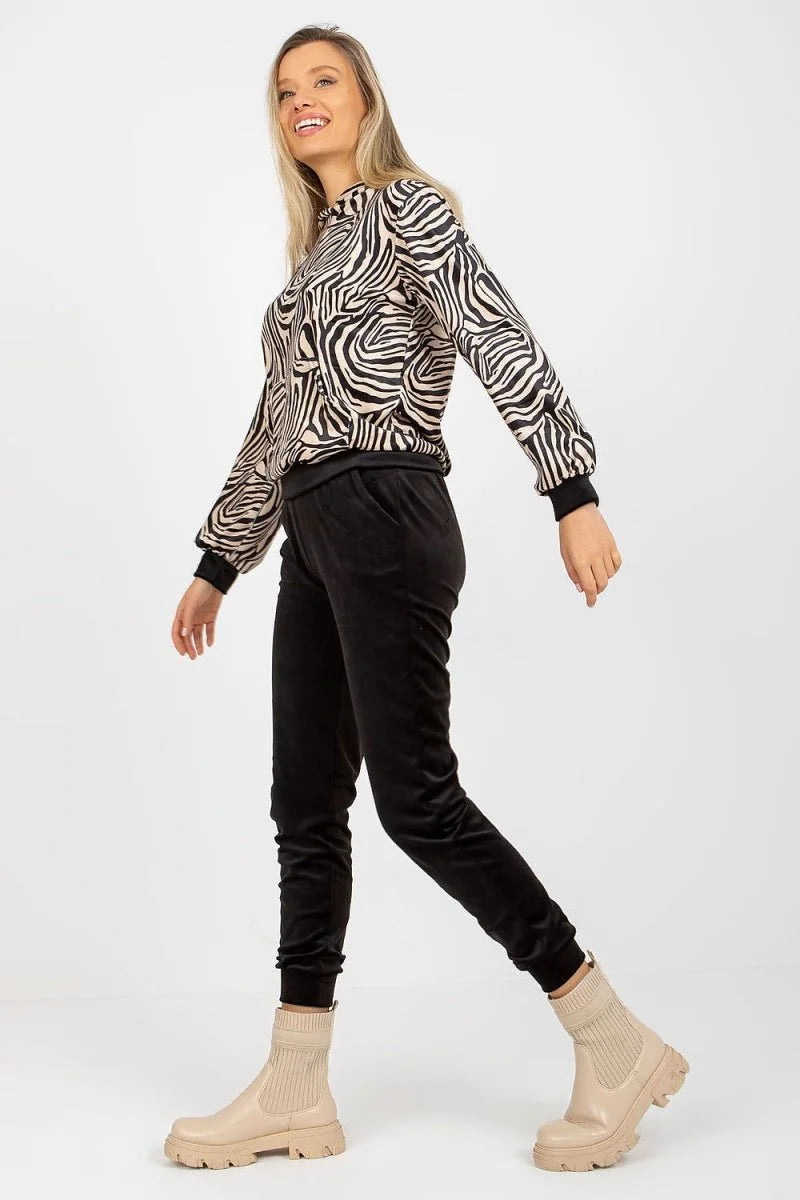 Woman in black velvet pants with a zebra print top and beige boots.