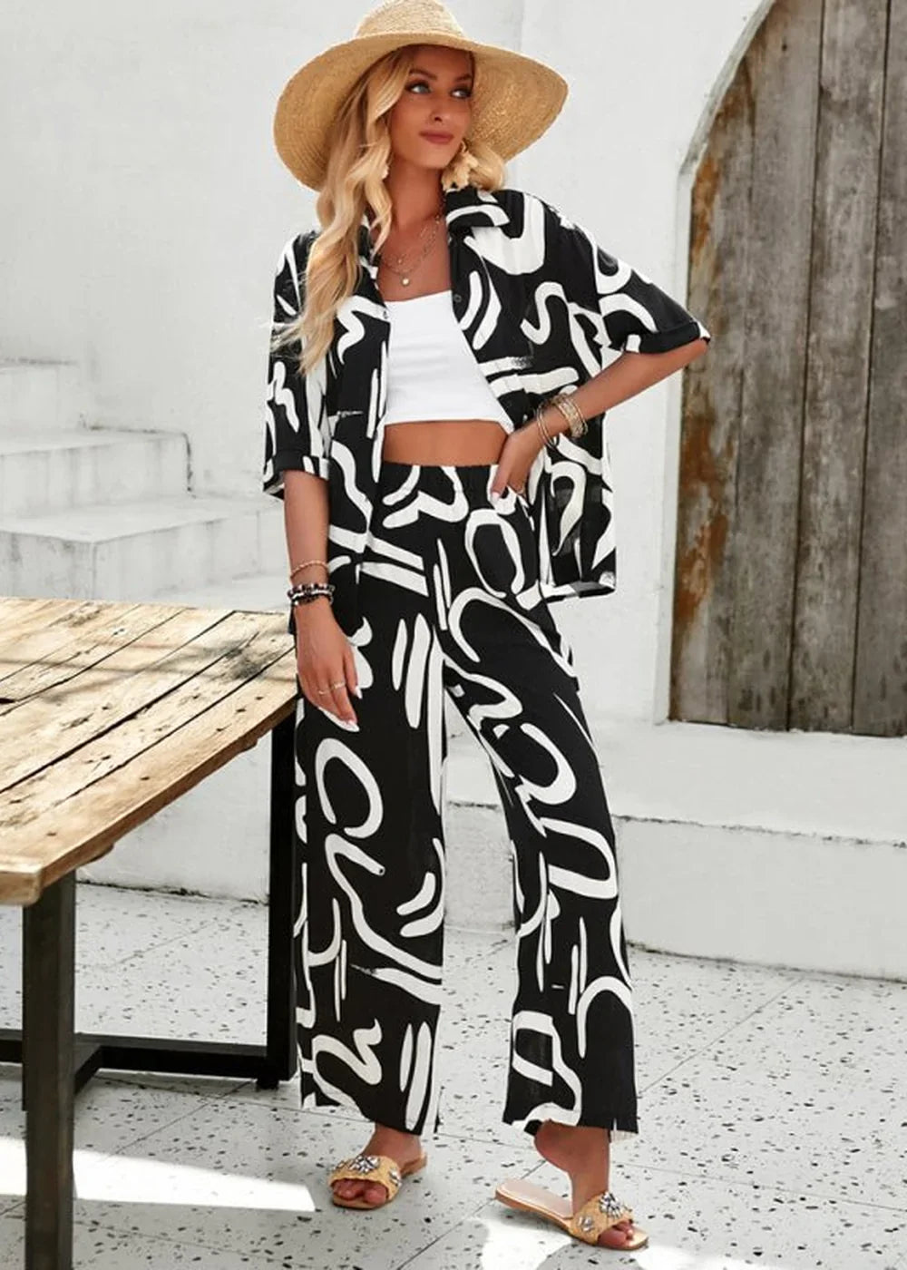 Black and white abstract print wide-leg pantsuit with straw hat and white crop top on model.