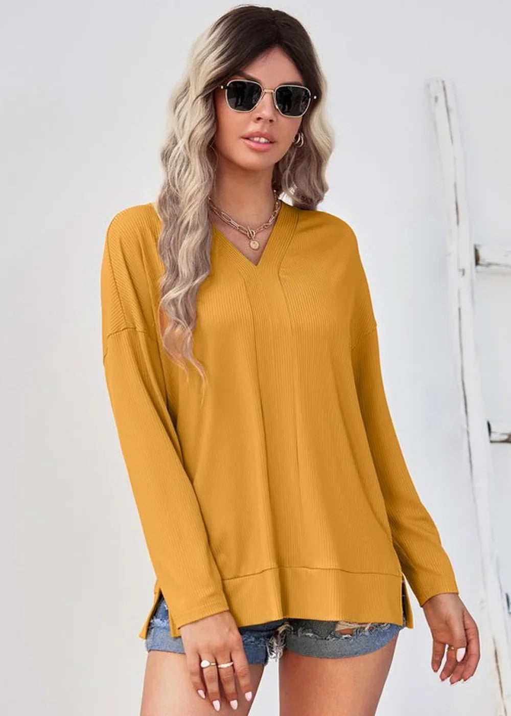 Woman in a mustard yellow ribbed v-neck long-sleeve top and denim shorts.