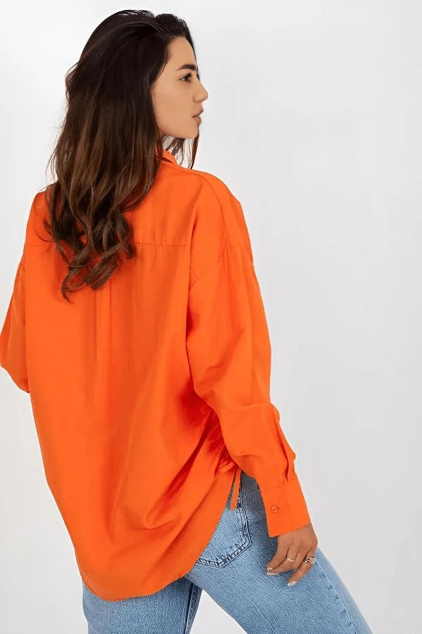 Woman from the back wearing a loose-fit, bright orange, long-sleeved cotton-blend button-down shirt and light blue jeans.