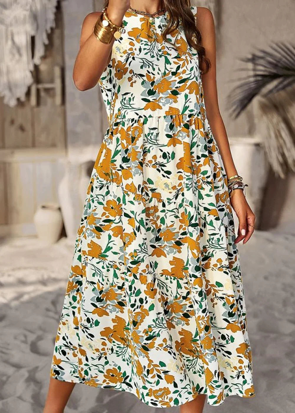 White sleeveless dress with a yellow and green floral print, tiered skirt, and gold bracelets.