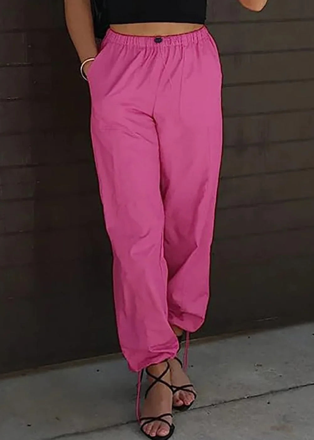 Bright pink jogger pants with drawstring ankles and tie-up sandals on model.