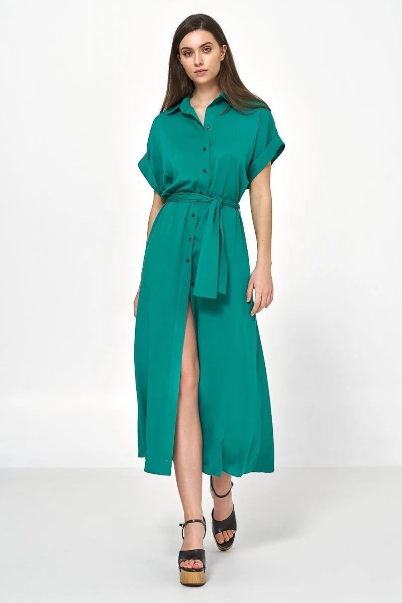 Woman in a flowing emerald green viscose midi shirt dress with a belted waist and high slit, wearing platform sandals.