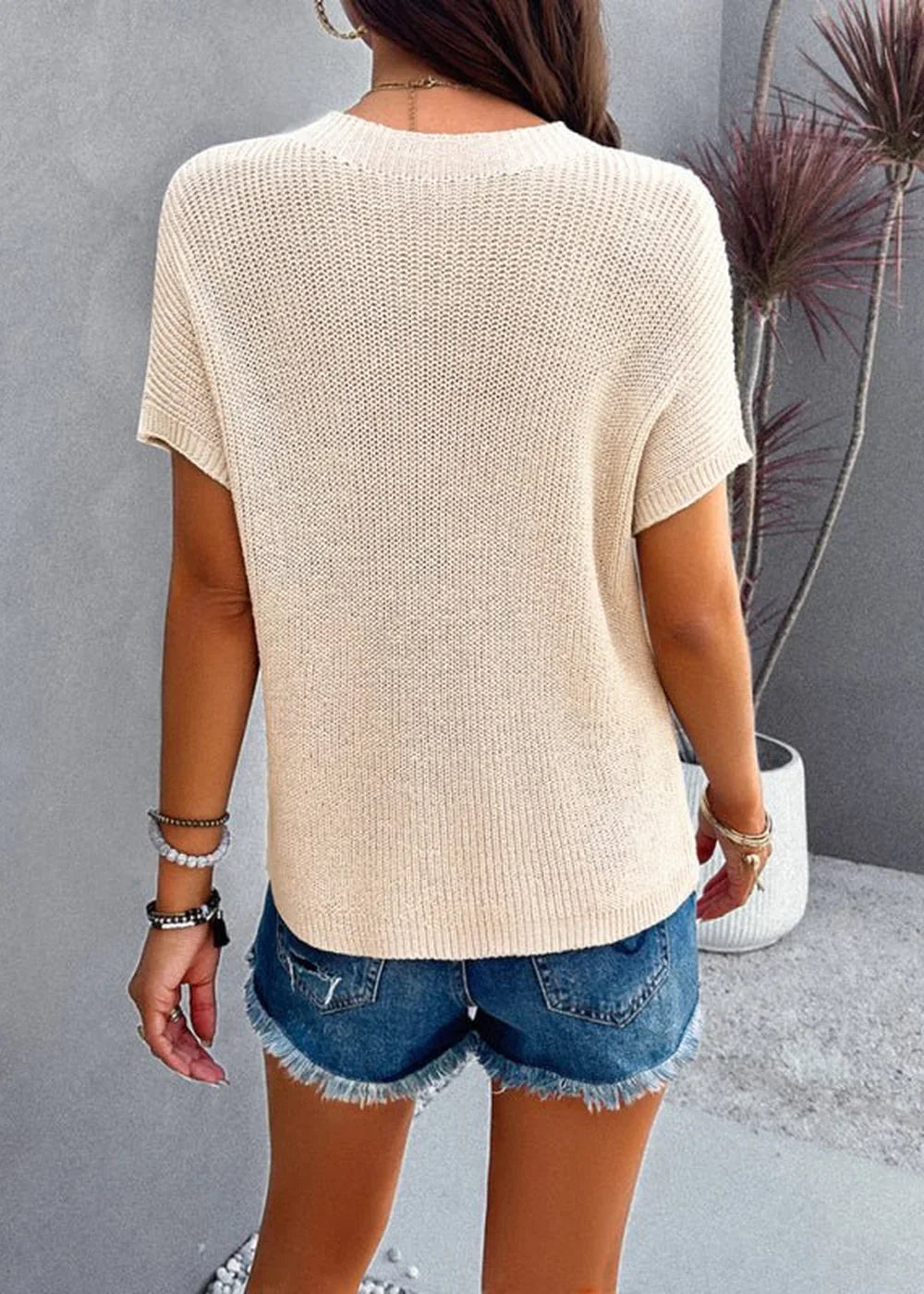 Back view of a cream-colored knit short-sleeve sweater on a model wearing denim shorts.