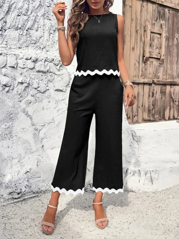 Black wide-leg jumpsuit with white scalloped trim, on model.