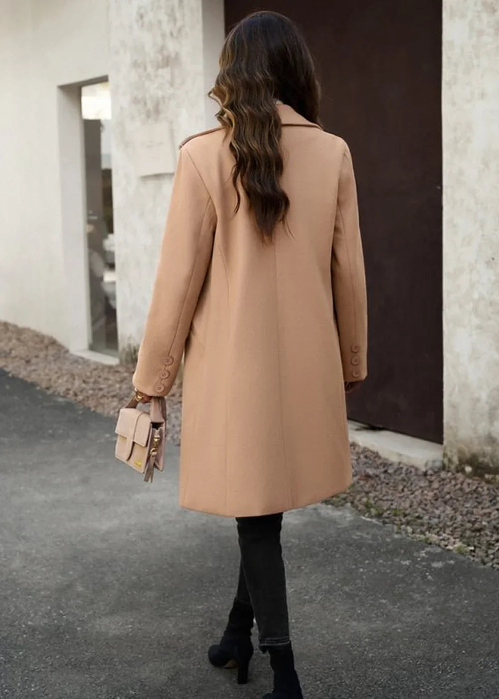 Camel coat with button details and a small beige handbag, shown from the back on a model.