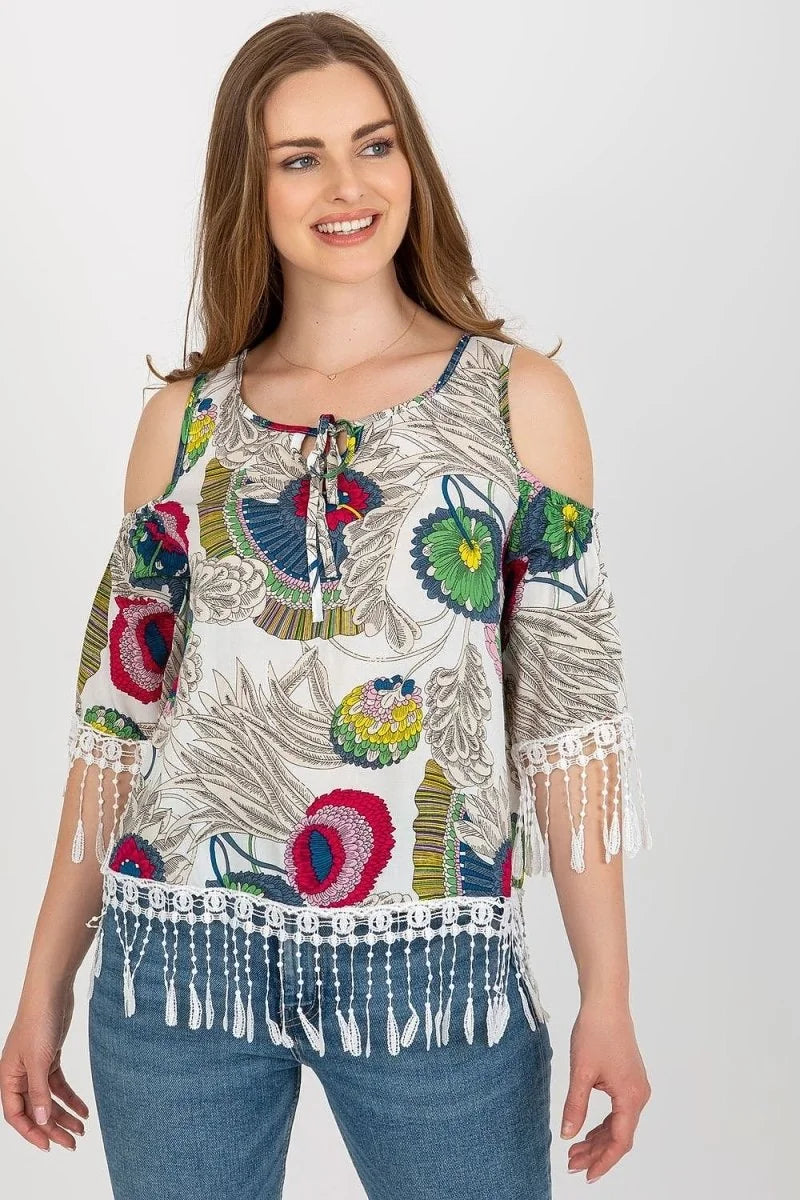 White cold-shoulder top with colorful floral print, tie-neck, and white fringe trim.