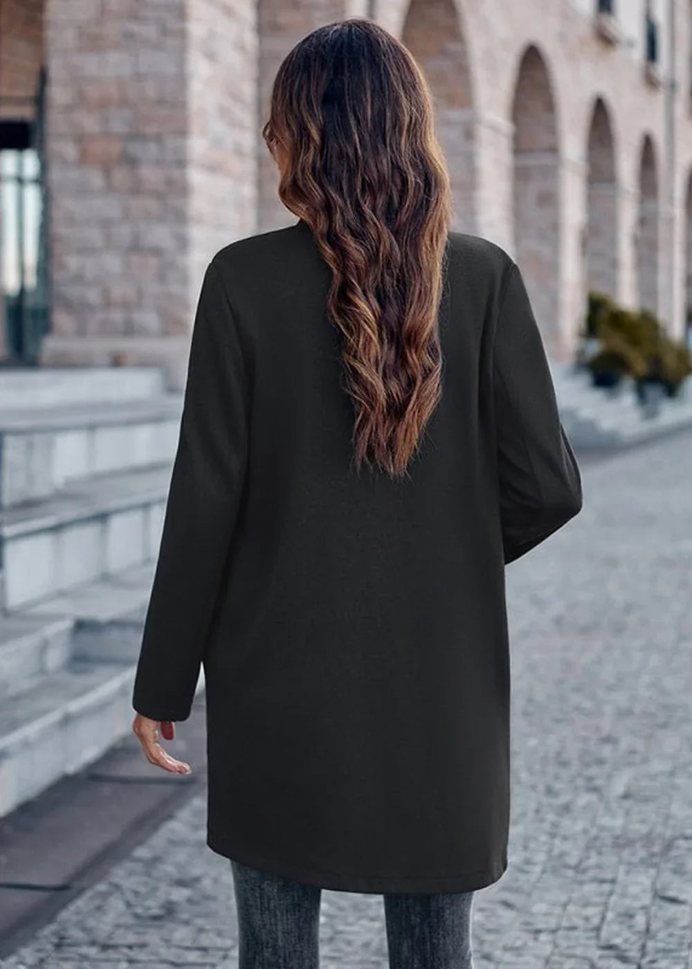 Back view of a woman wearing a plain black long-sleeved jacket over jeans.