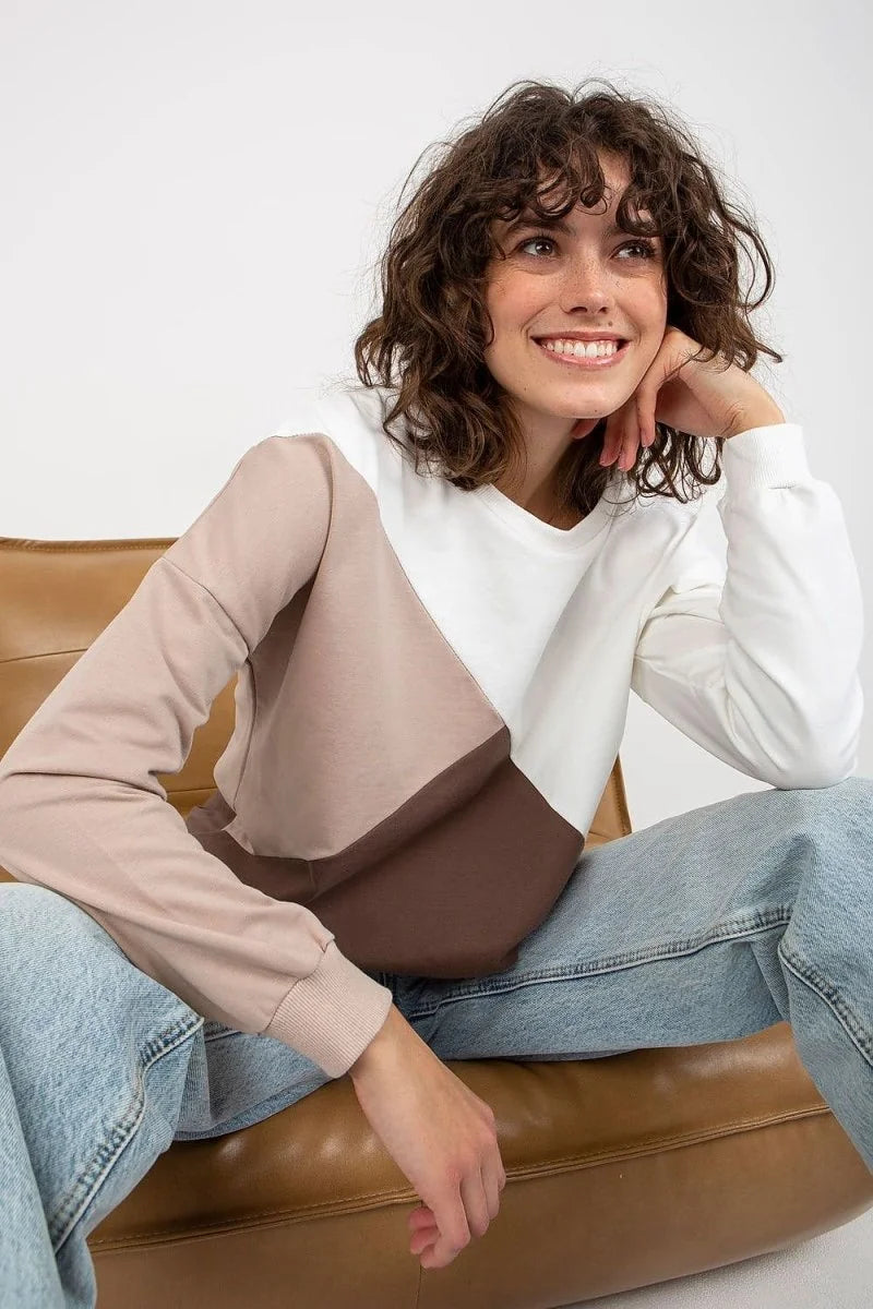 Woman in a colorblock sweatshirt with brown, taupe, and white panels, wearing light wash denim.