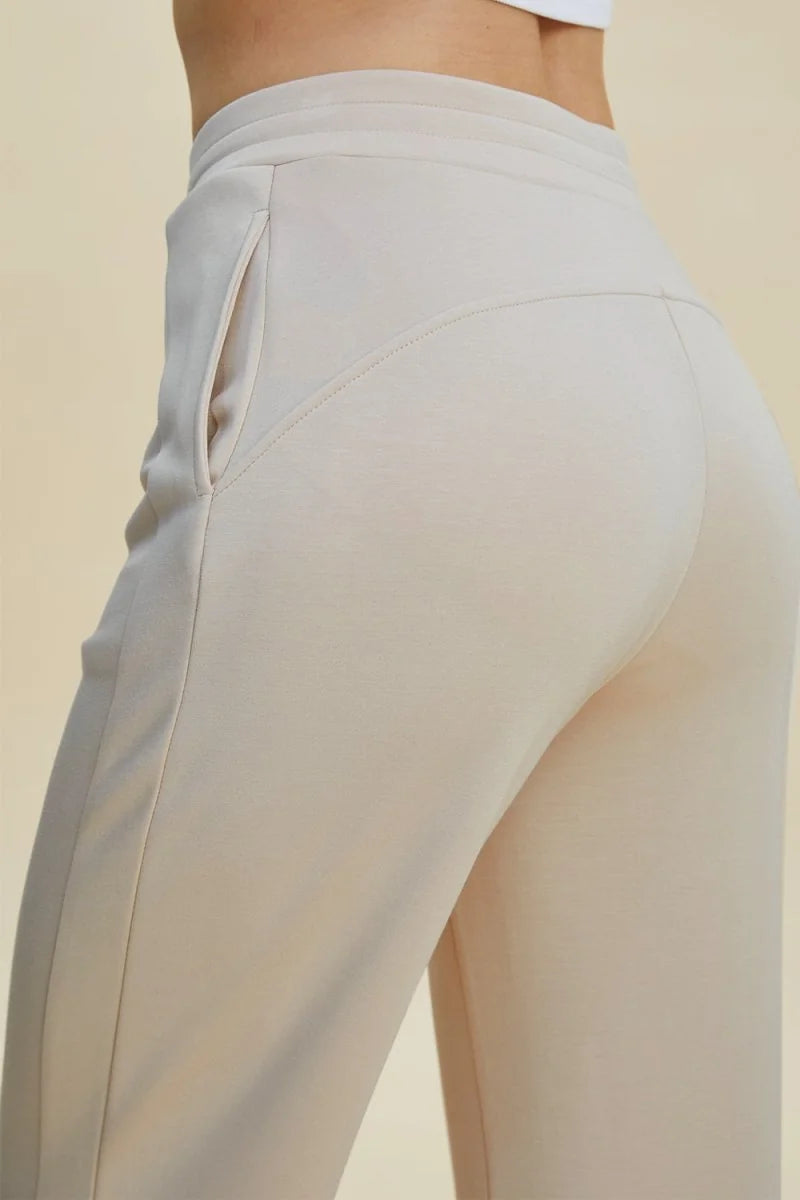 Close-up of beige sweatpants with a relaxed fit, featuring a side pocket and curved seam detail.