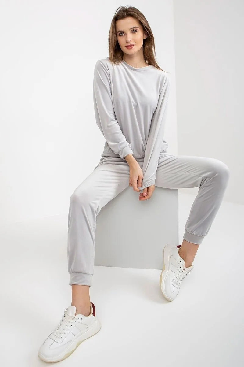 Light grey velour tracksuit with white sneakers on a seated model.