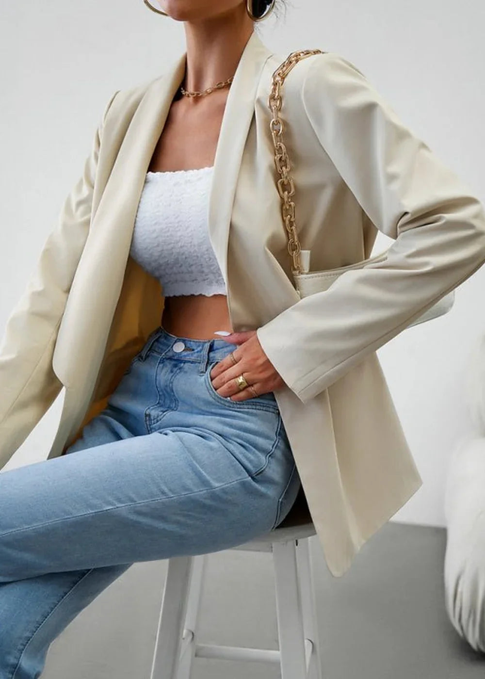 Cream-colored blazer with a textured white bandeau top and light wash denim jeans.