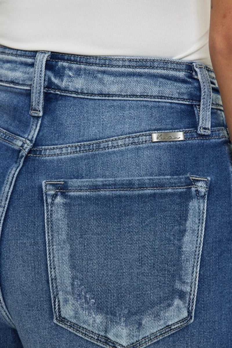 Close-up of distressed medium wash denim jeans with a silver logo accent.