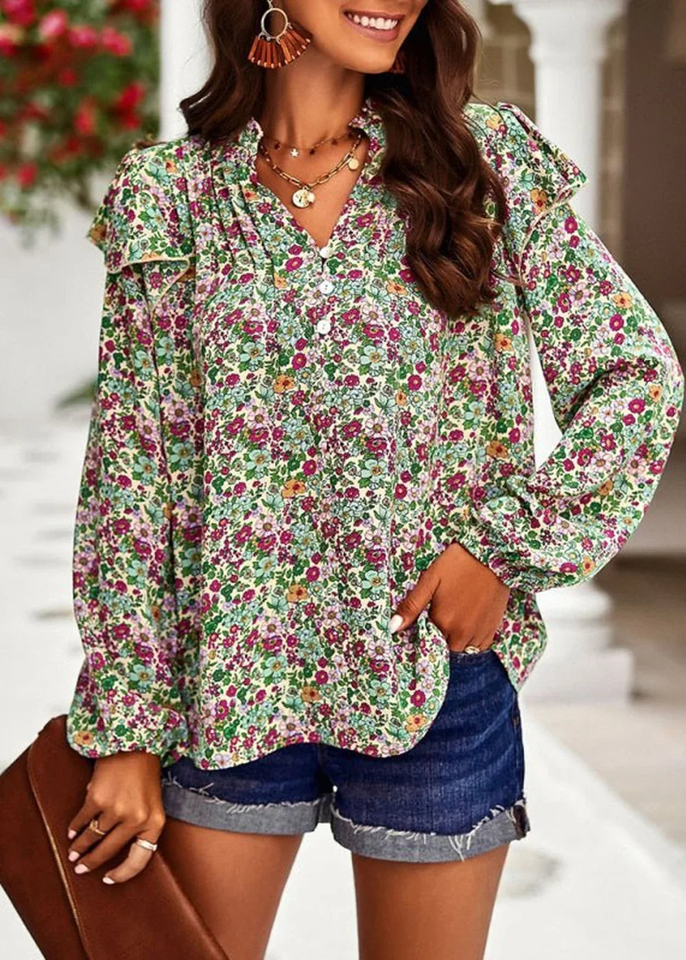 Woman in a colorful floral print blouse with ruffle details and denim shorts, holding a brown clutch.