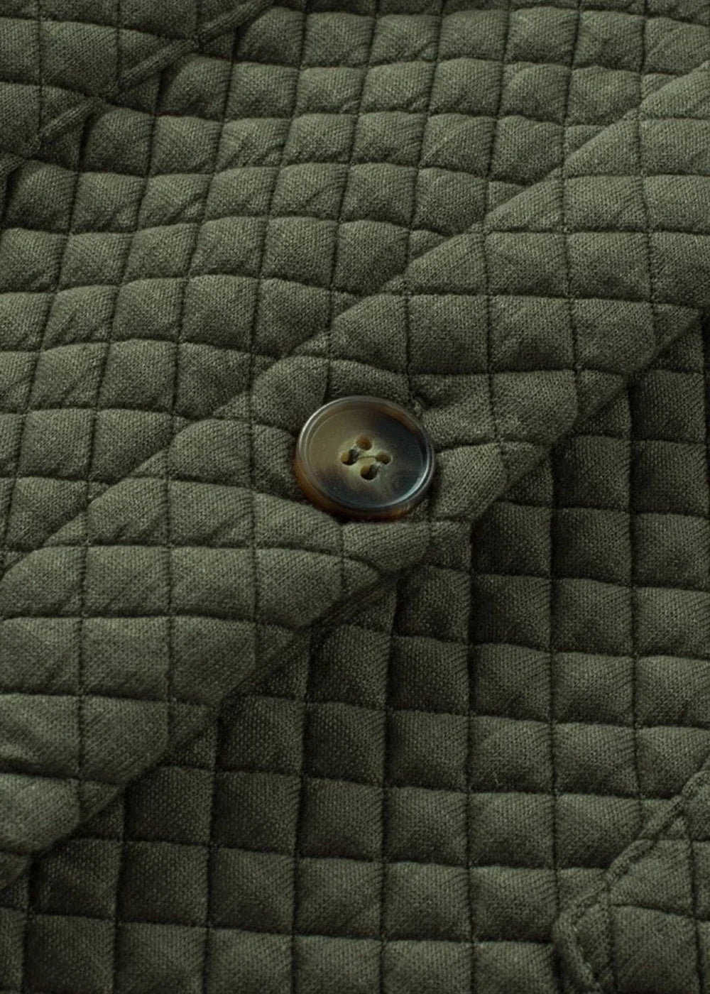 Close-up of a dark olive green quilted jacket with a single brown button closure.
