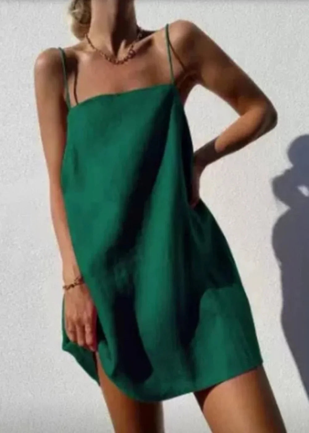 A model wears a loose, emerald green cotton-linen mini dress with thin spaghetti straps.
