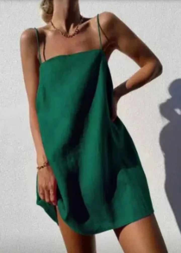 A model wears a loose, emerald green cotton-linen mini dress with thin spaghetti straps.