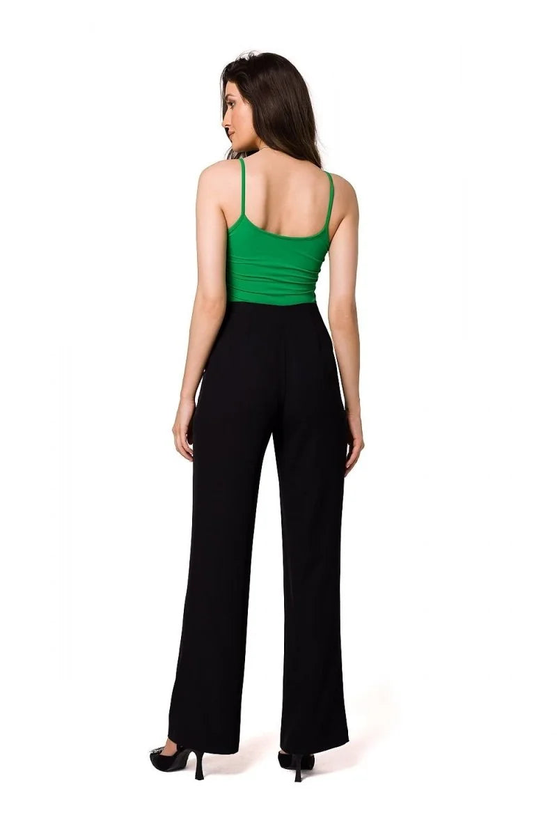 Back view of a woman wearing high-waisted black palazzo pants and a green camisole.