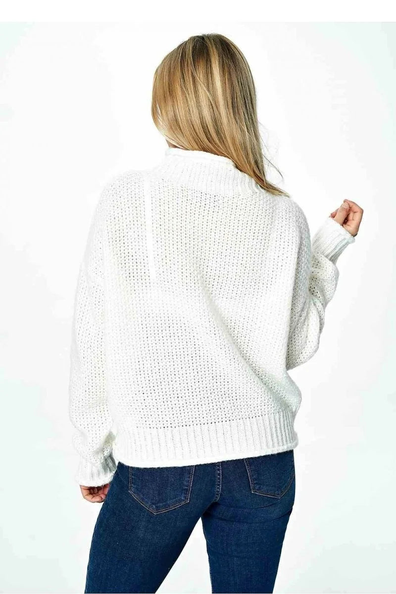 Back view of a woman wearing a white chunky knit turtleneck sweater and dark wash jeans.
