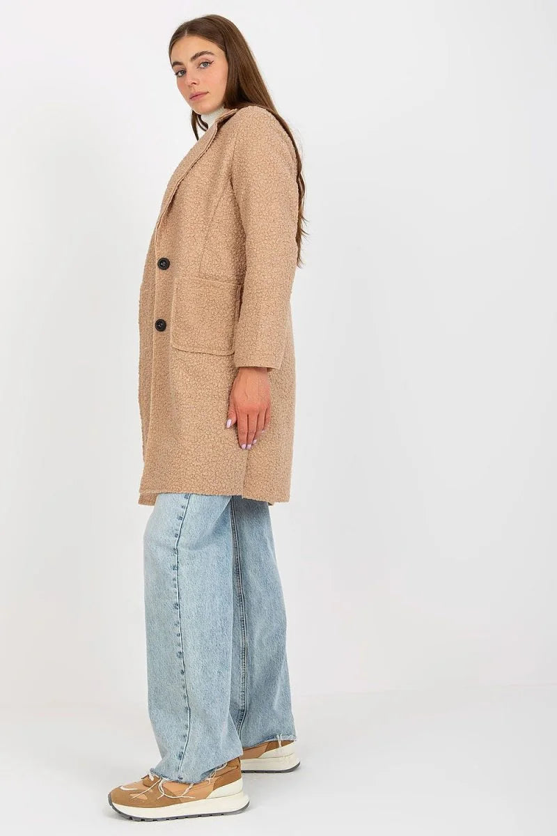 Woman in a textured beige coat and light blue wide-leg jeans, side view.