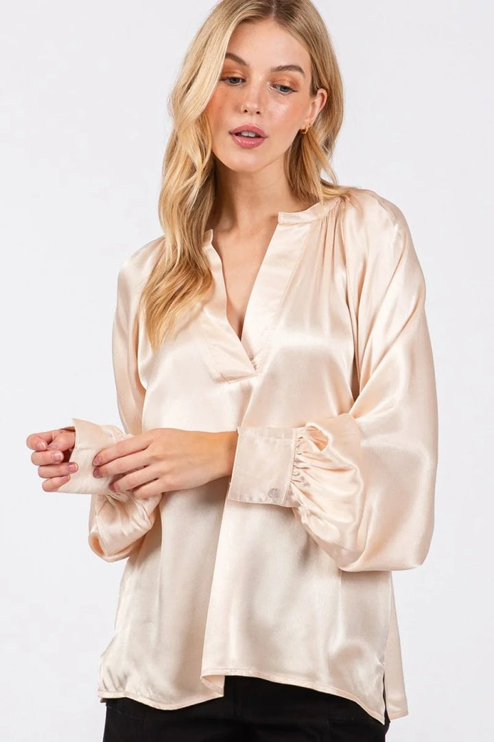 Cream satin blouse with V-neck, relaxed fit, and ruffled cuffs.
