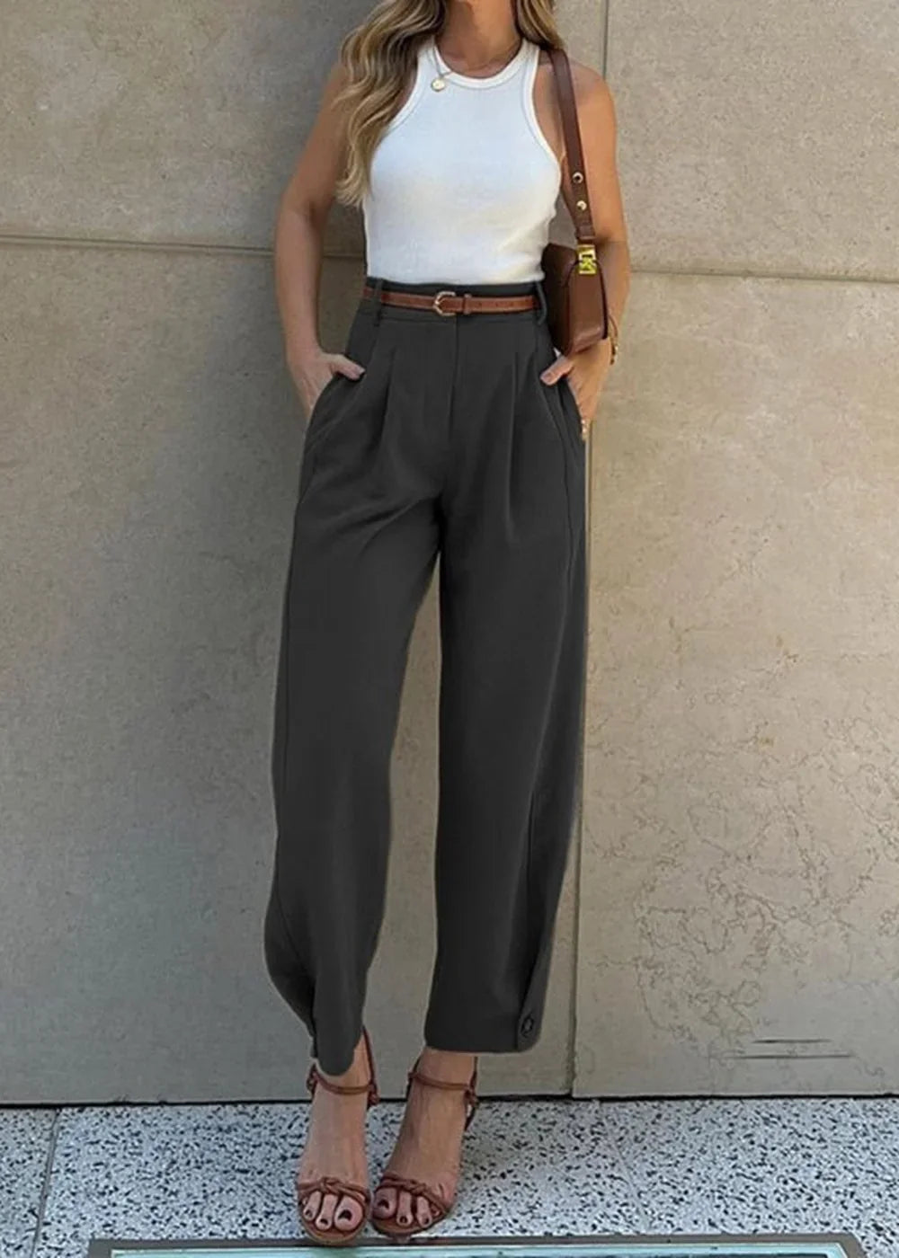 Woman wearing a white ribbed tank top, charcoal grey wide-leg pants with a brown belt, and brown heeled sandals.