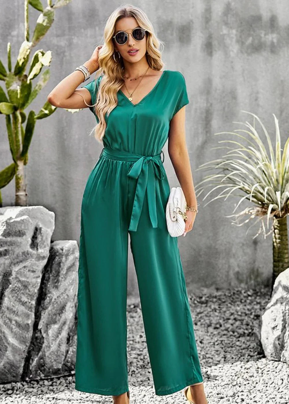 Emerald green satin jumpsuit with V-neck, tie waist, and wide legs, worn by a model outdoors.
