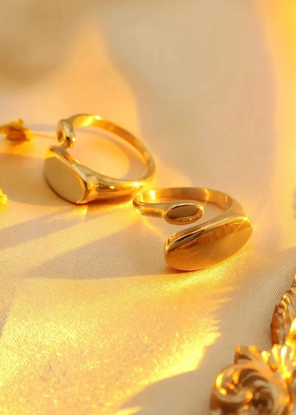 Gold-plated titanium steel rings with smooth, polished surfaces arranged on a textured, cream-colored fabric.