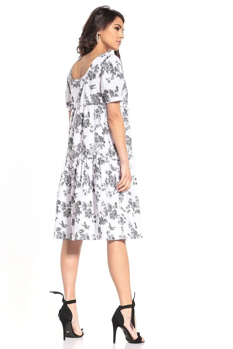White cotton dress with black floral pattern, relaxed fit, tiered skirt, on model with black heels.
