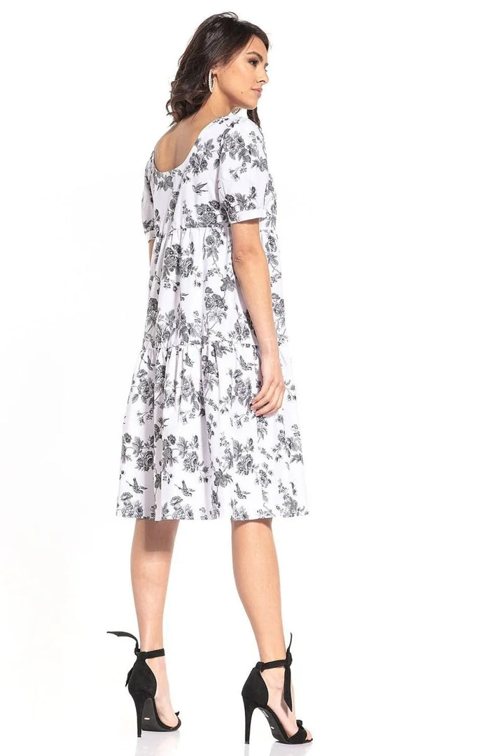 White cotton dress with black floral pattern, relaxed fit, tiered skirt, on model with black heels.