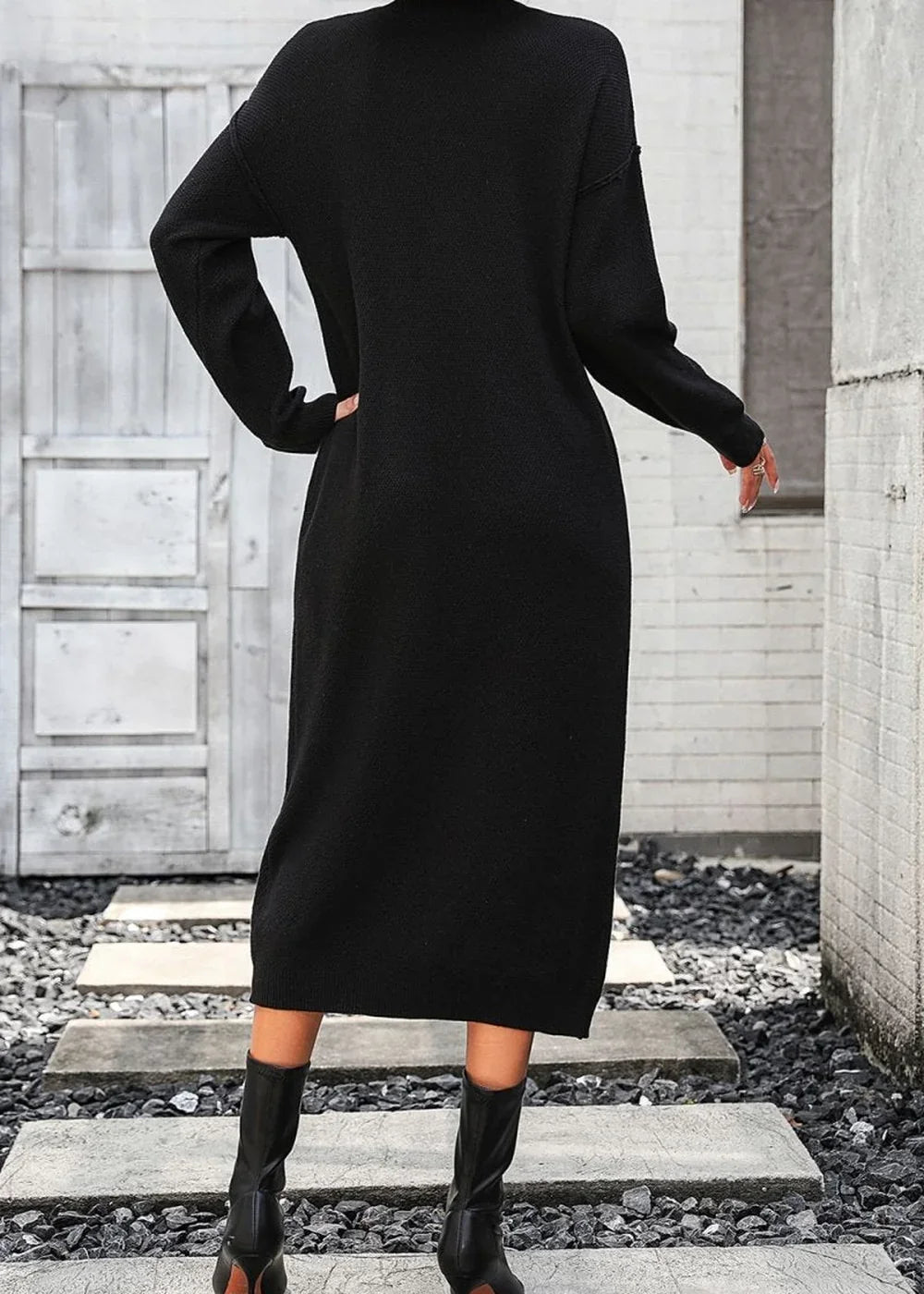 Back view of a black acrylic blend sweater dress with a high neckline, worn with black boots.