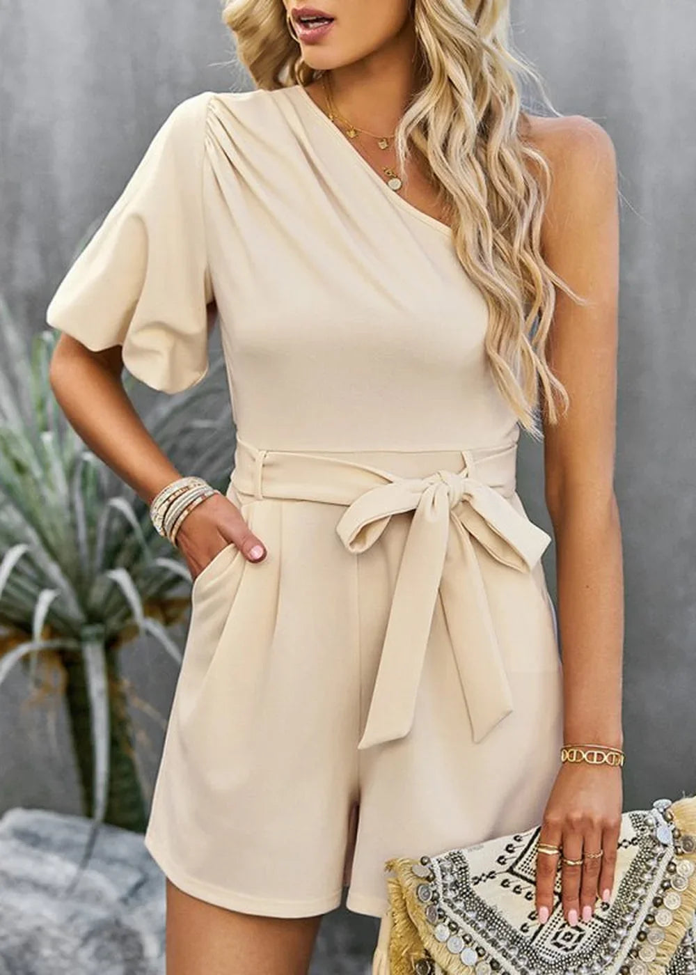 Cream one-shoulder romper with puff sleeve, self-tie waist, and pockets.
