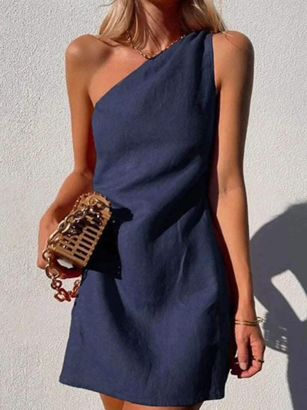 Navy blue one-shoulder mini dress with gold chain detail and a woven clutch.