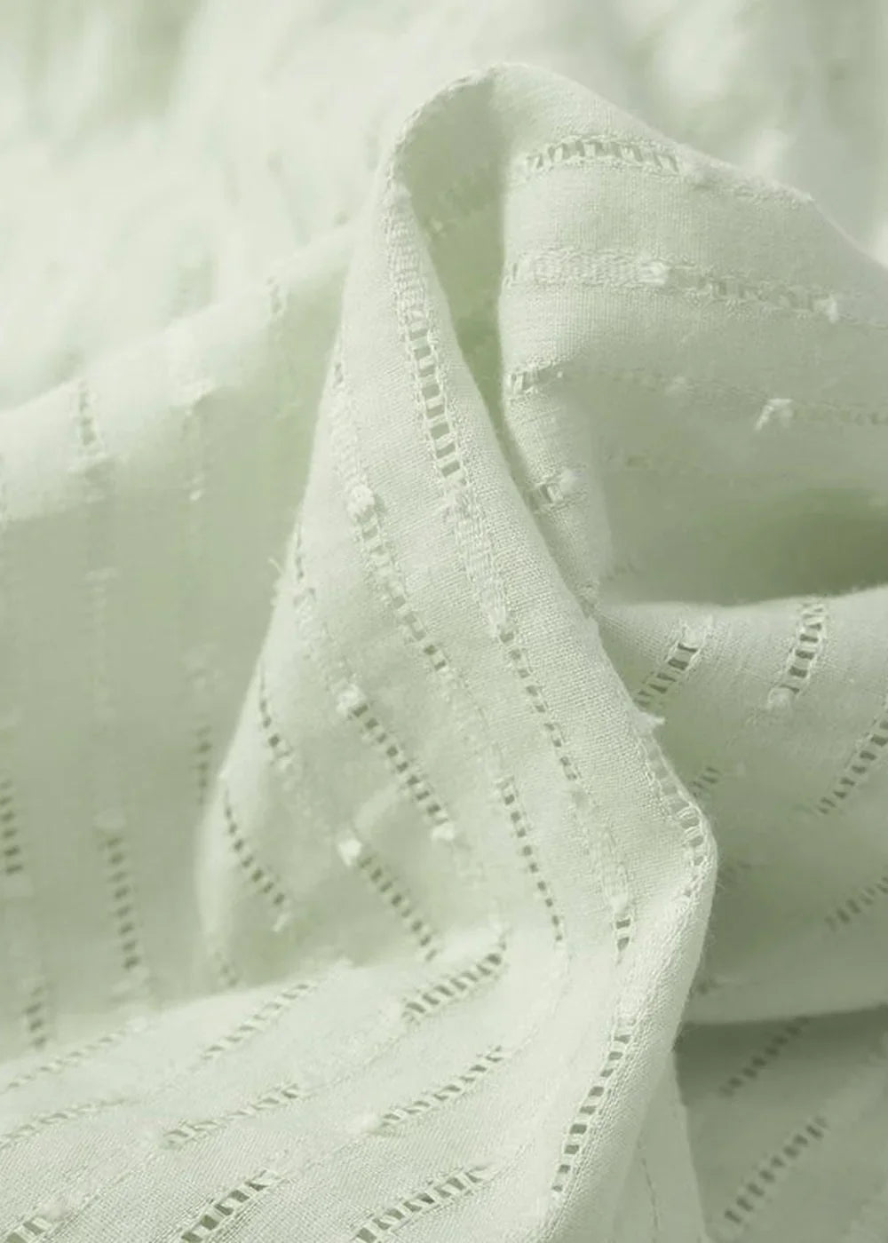 Close-up of a light green cotton fabric with a subtle textured stripe and dotted pattern.