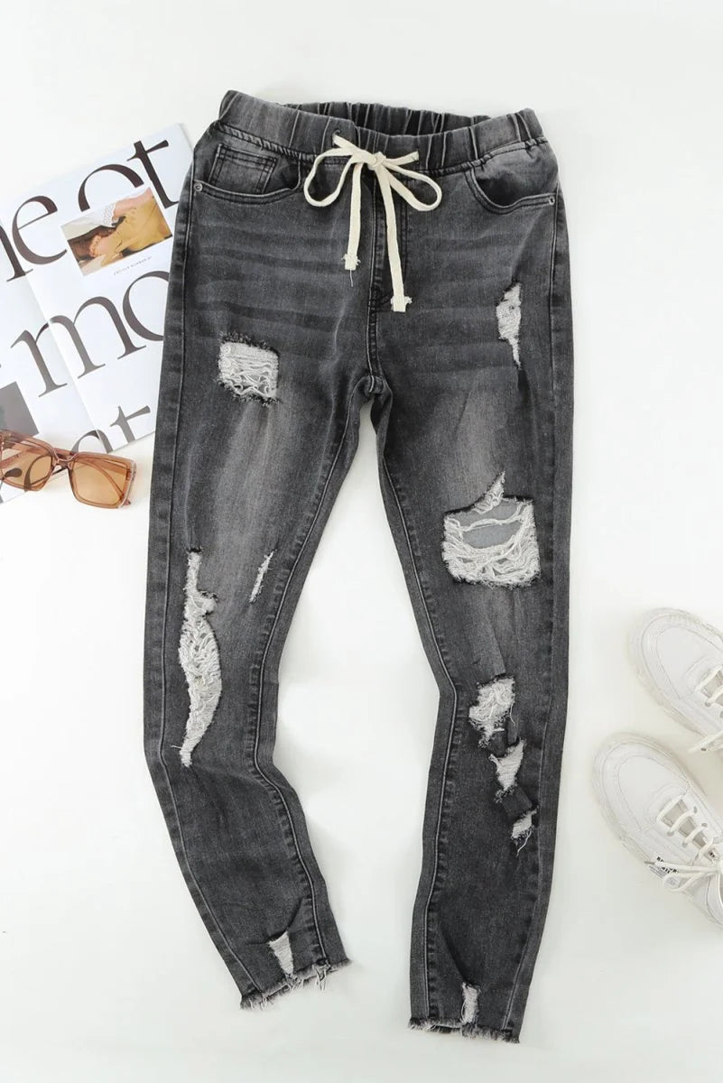 Distressed charcoal gray denim joggers with a frayed hem and drawstring waist.