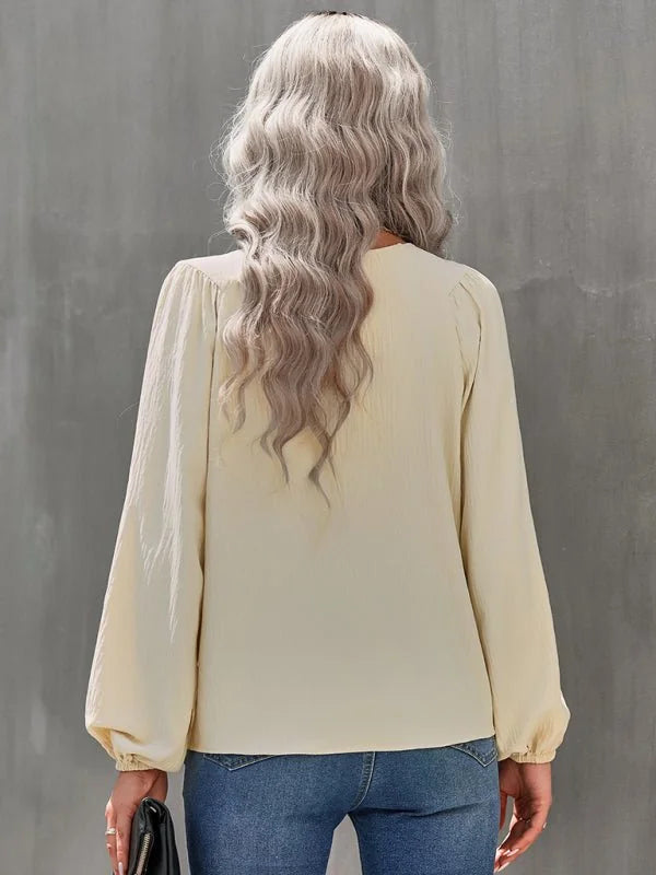 Back view of a cream textured blouse with long balloon sleeves, worn by a model with wavy blonde hair over blue jeans.