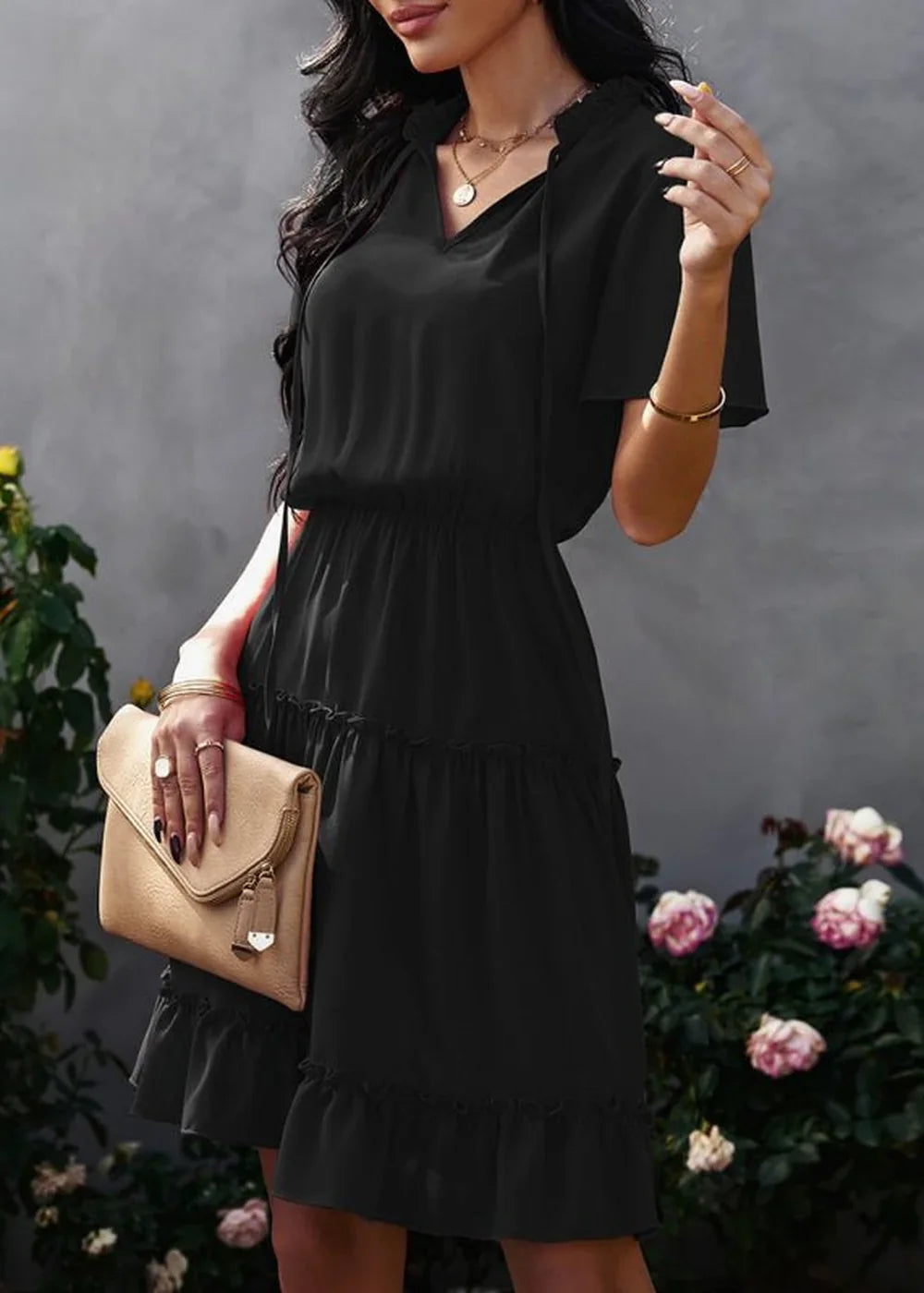 Black ruffled v-neck midi dress with cinched waist, held beige clutch, on model