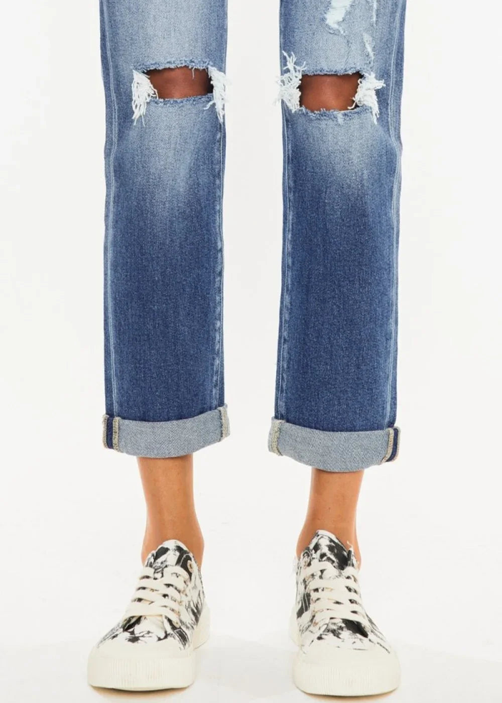 Distressed blue denim jeans with cuffed hems and white and black abstract print sneakers.