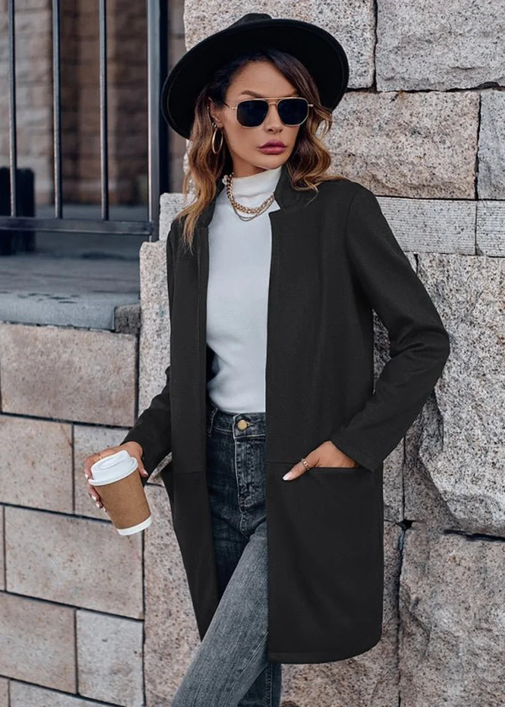 Black open-front blazer with pockets, worn by a model with a white turtleneck and jeans.